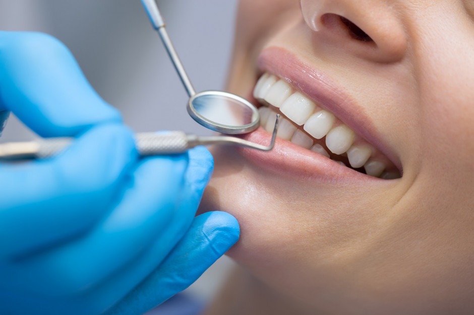 Zbliżenie na uśmiechniętą pacjentkę podczas badania stomatologicznego – dentysta sprawdza zęby przy użyciu lusterka i sondy.